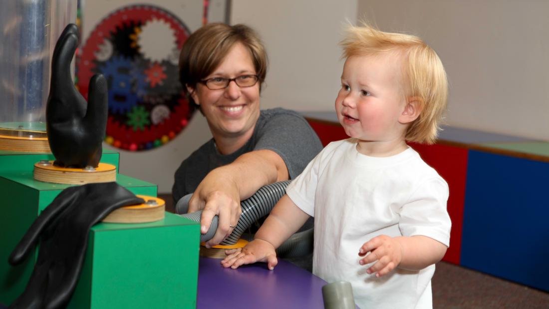 Adult man with a young blonde toddler play with inflatables on a green and purple table at the Fleet Science Center