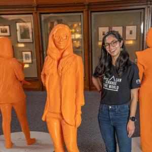 A woman stands next to an orange statue of herself