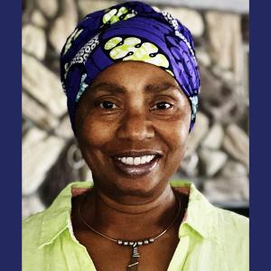 A black woman in a green top and purple head wrap smiling 