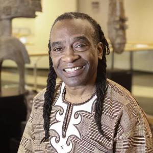 A black man in a brown top smiling in a museum artifact setting 
